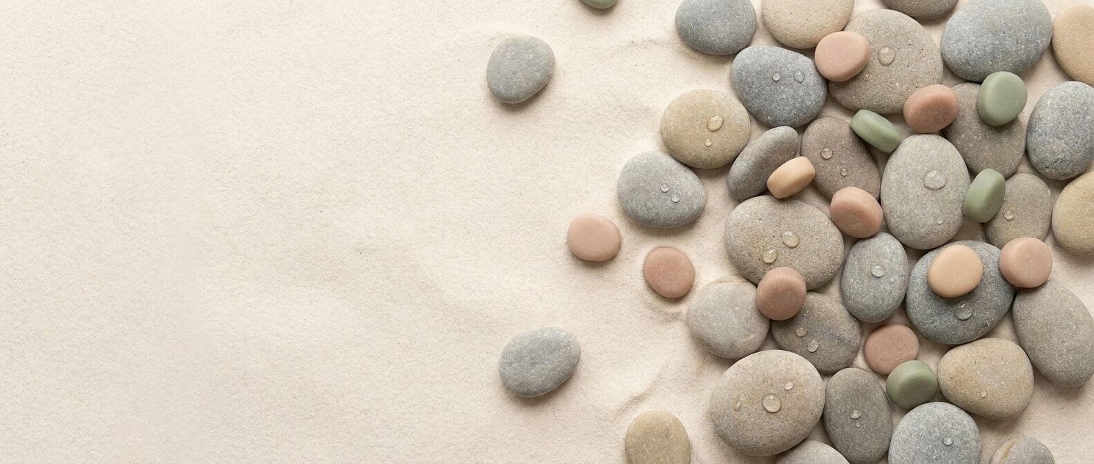 Smooth grey river stones on pale sand with pink, sand and sage gummies tucked among them.